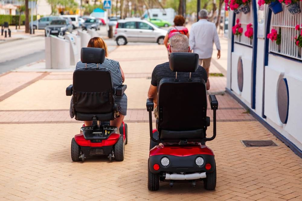 couple riding mobility scooters on sidewalk