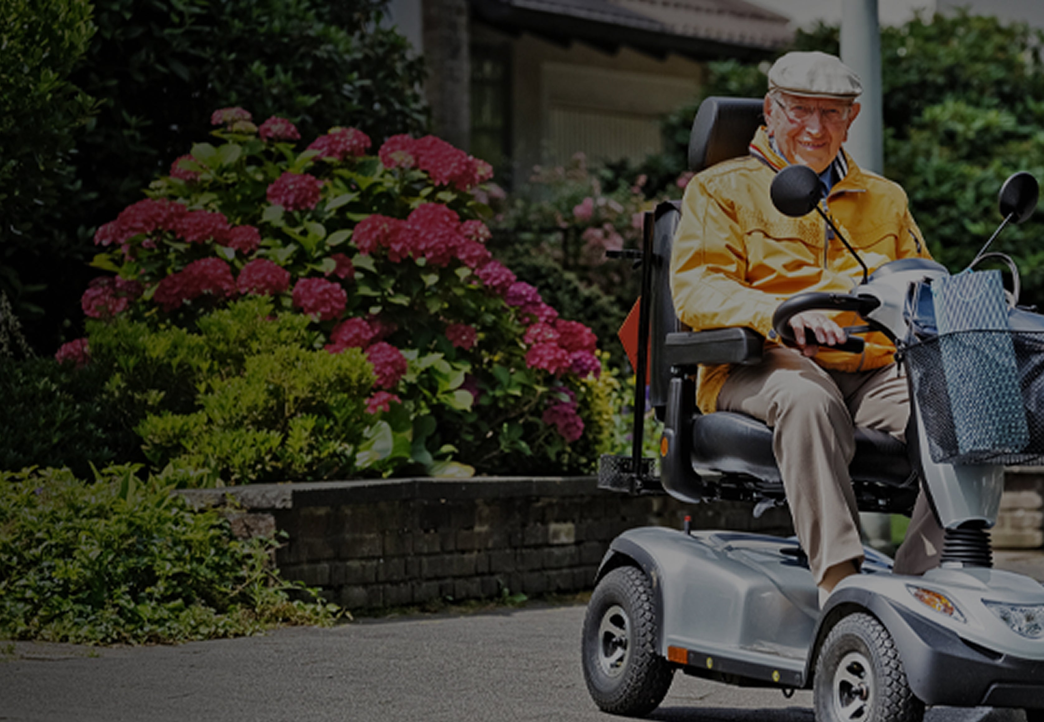 Man in a yellow raincoat using a mobility scooter in a garden setting