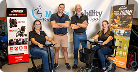 Group of people with mobility scooters in front of a Marcs Mobility banner.
